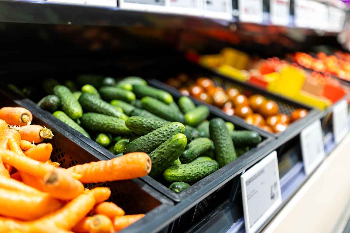 Pirkėjų matomi švieži morkų ir agurkų krūvos prekybos centre
